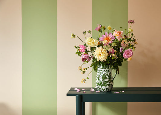 Green and nude striped painted wall with black table and springtime flowers in a vase