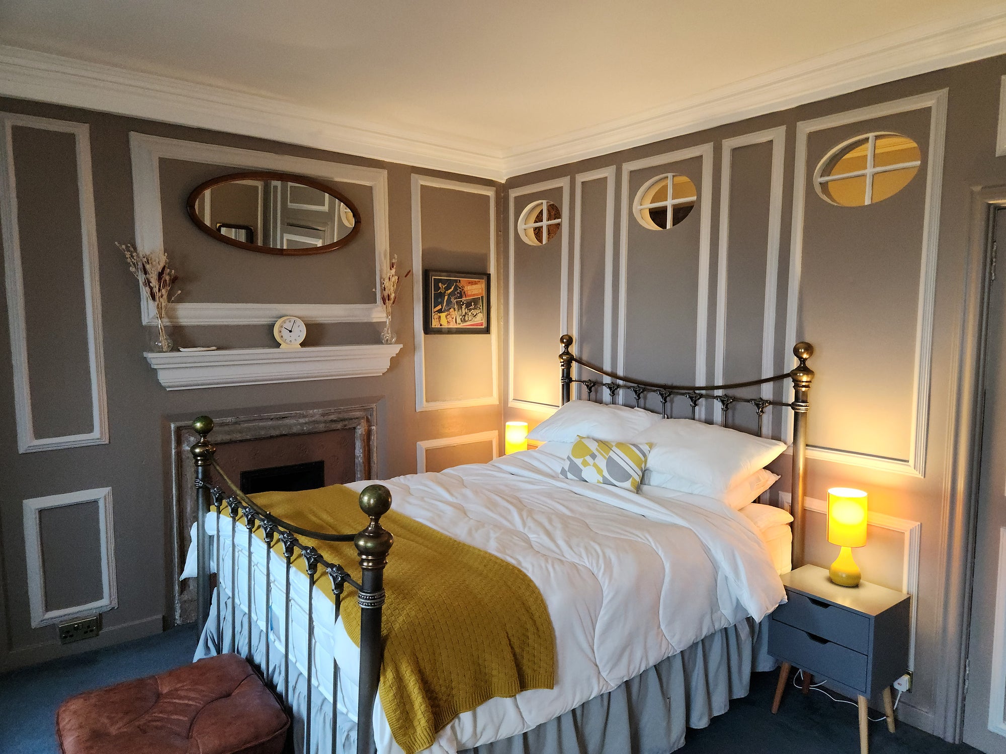 Traditional grey painted bedroom with white moulding detailing. Gold bed with white duvet and yellow blanket.