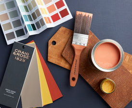 Craig & Rose premium paint colour card, paint fan deck, paint brush and sample pots of red and yellow paints on a blue background