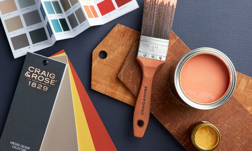 Craig & Rose premium paint colour card, paint fan deck, paint brush and sample pots of red and yellow paints on a blue background