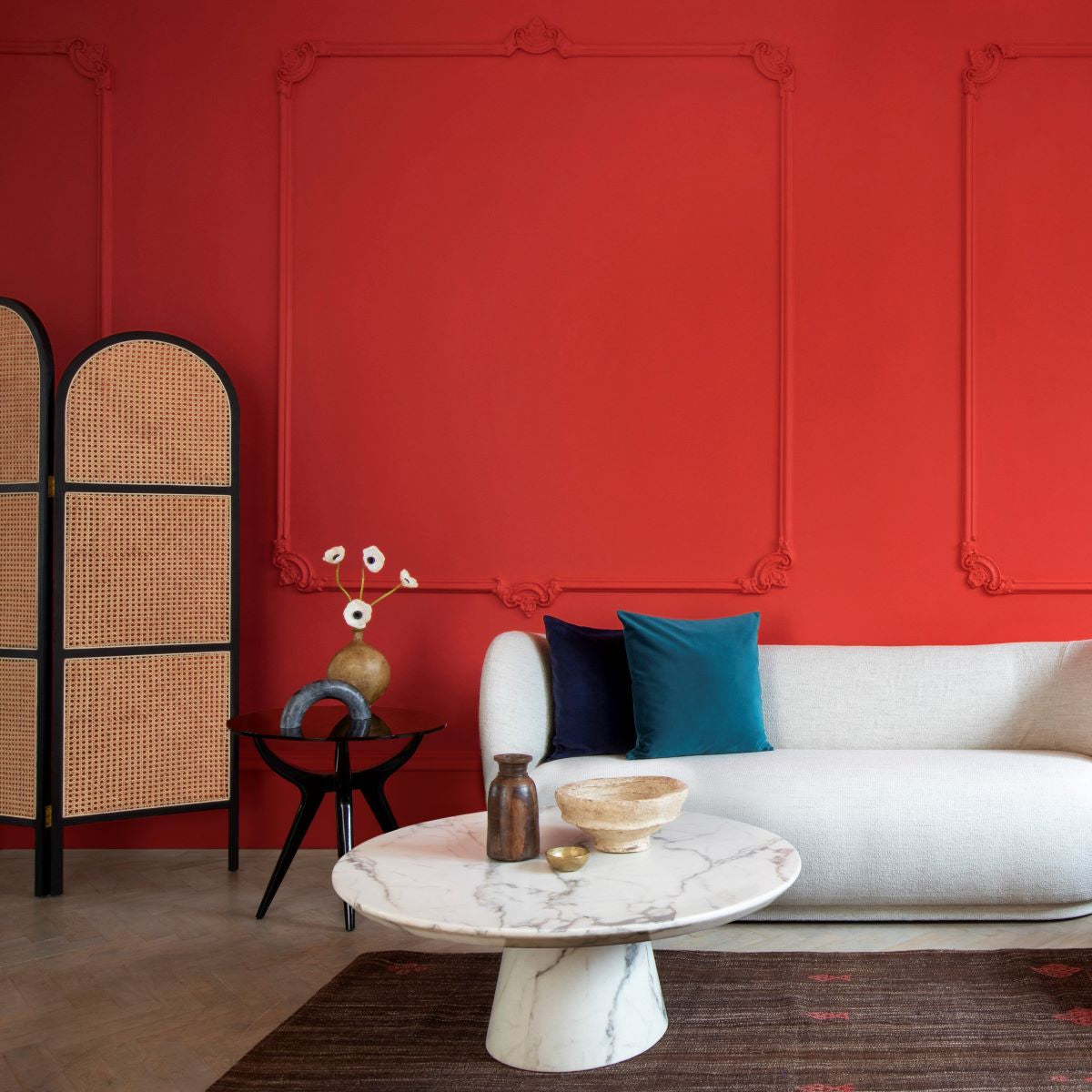 Modern Troubadour red painted room with white sofa, blue cushions, a white marble table and jute rug.